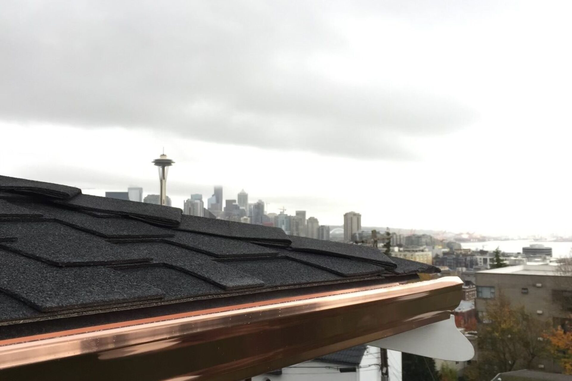 Copper gutter installation on a residential roofline with Seattle skyline in the background